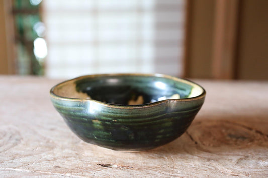 A ceramic bowl with a green and black glaze sits on a wooden surface.