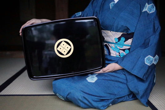 A person wearing a blue kimono with a black tray featuring a gold and black design.