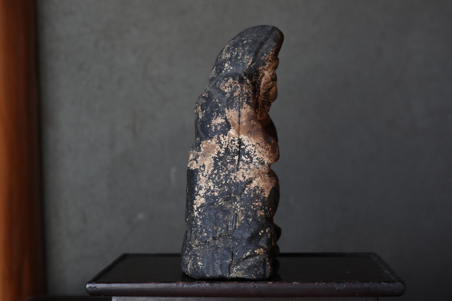 a dark, weathered statue of a person, possibly a religious figure, sitting on a small wooden table.