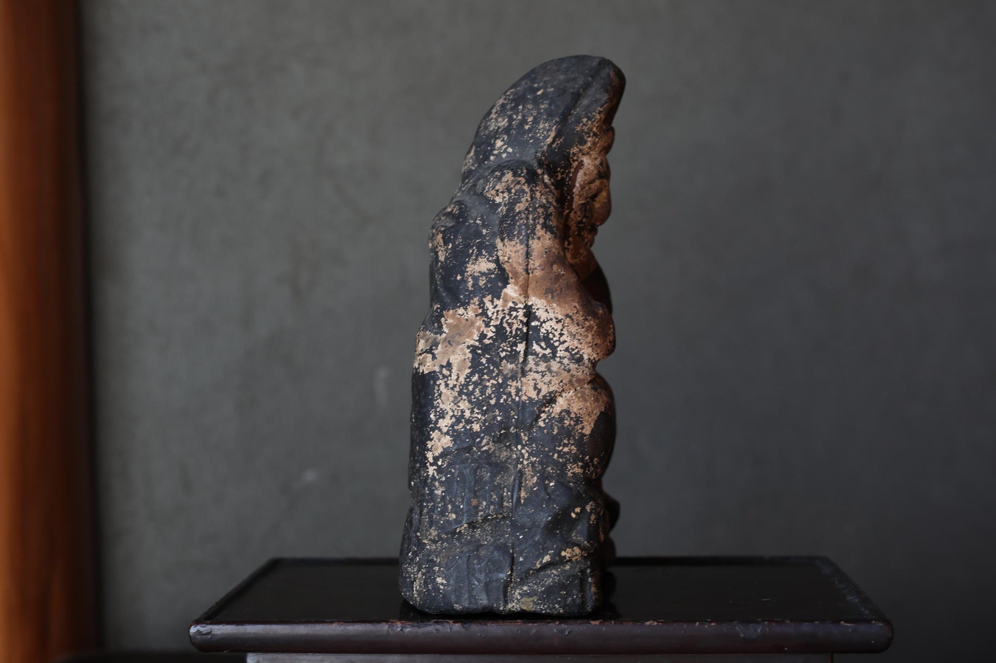a dark, weathered statue of a person, possibly a religious figure, sitting on a small wooden table.