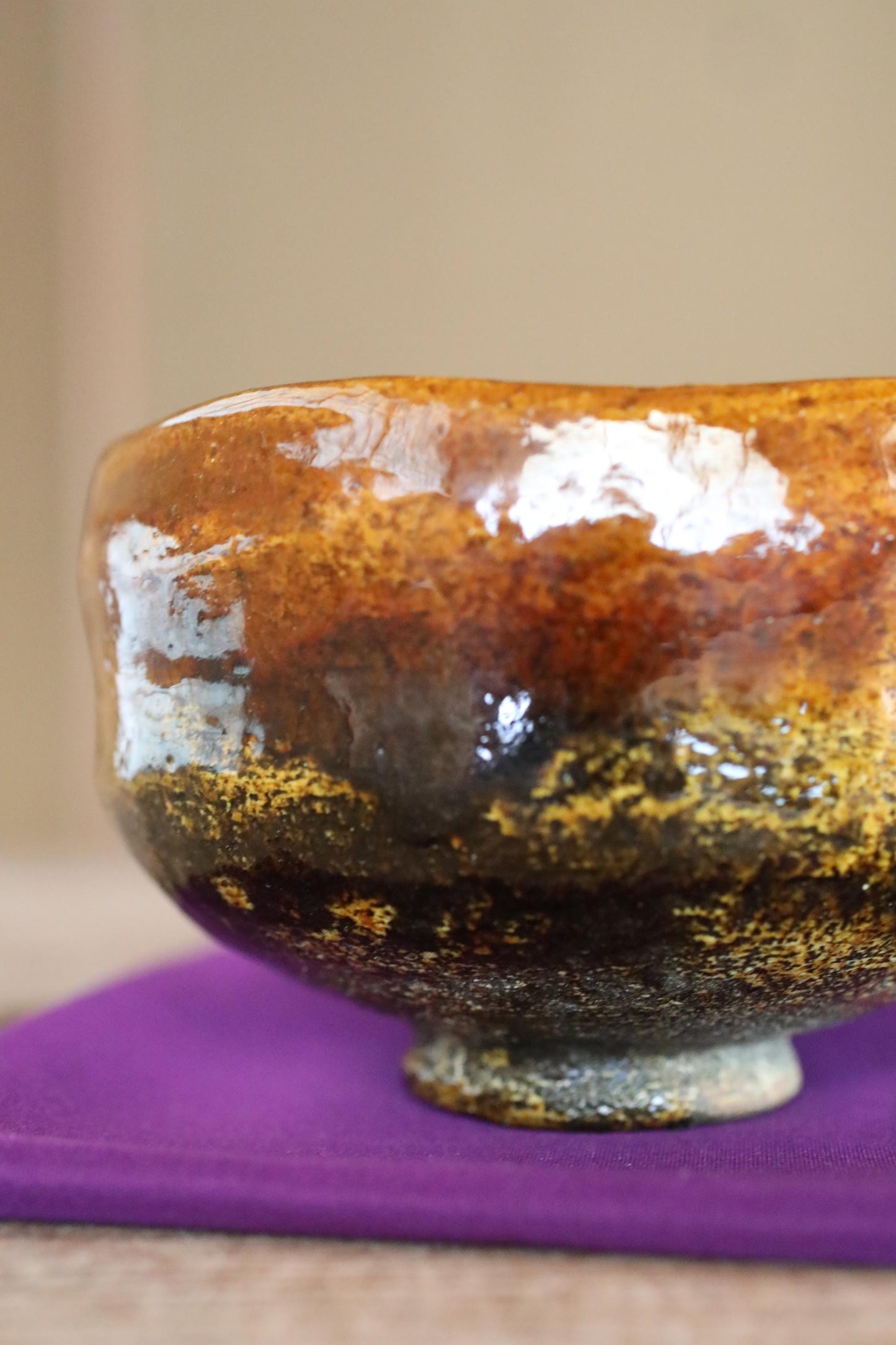 A close-up view of a ceramic mug or bowl with a textured surface, featuring a combination of brown, orange, and black colors.