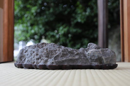 A large, gray rock sits on a wooden base, placed on a wooden surface.
