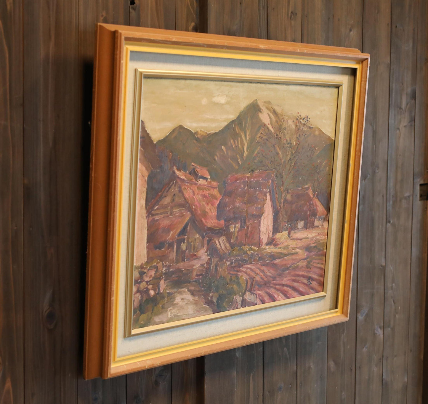 a framed painting of a rural landscape with mountains in the background.
