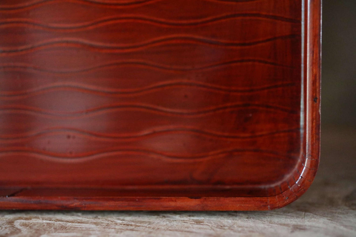 A close-up view of a wooden tray with a wavy pattern, showcasing the natural texture and grain of the wood.