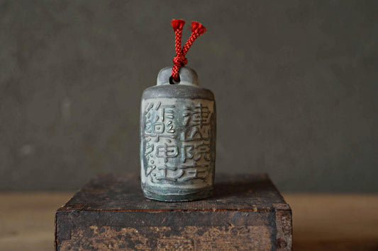 A ceramic bell with Chinese characters on it, placed on a wooden surface against a gray background.