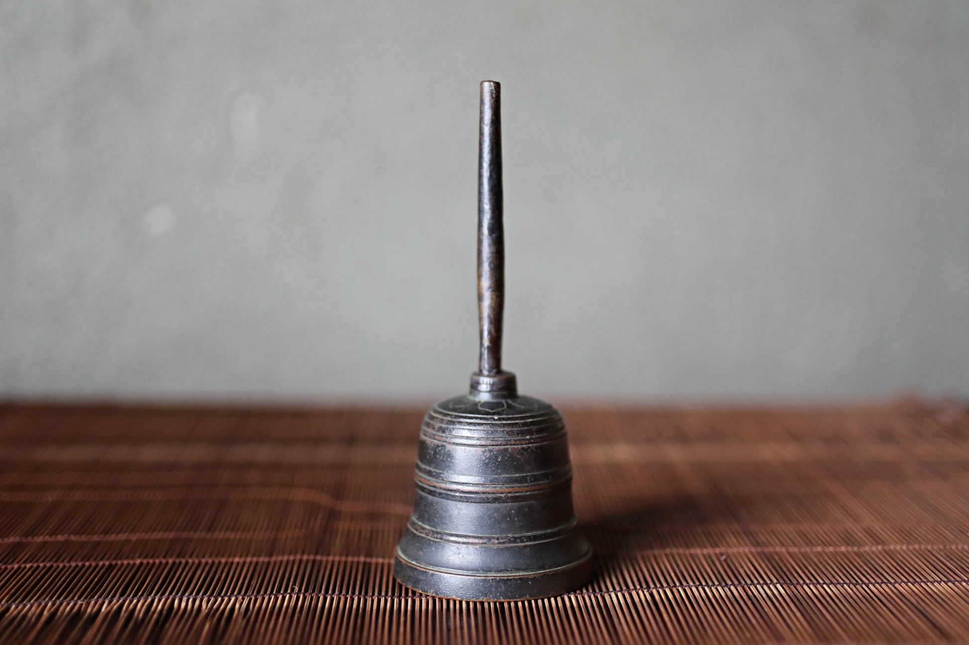A metal bell with a long, thin handle is sitting on a wooden surface.