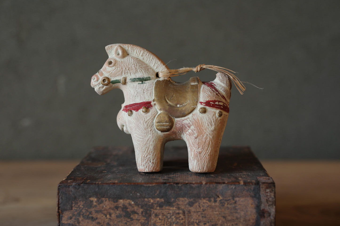 A small, white ceramic horse figurine with a red and green ribbon around its neck is displayed on a wooden surface.