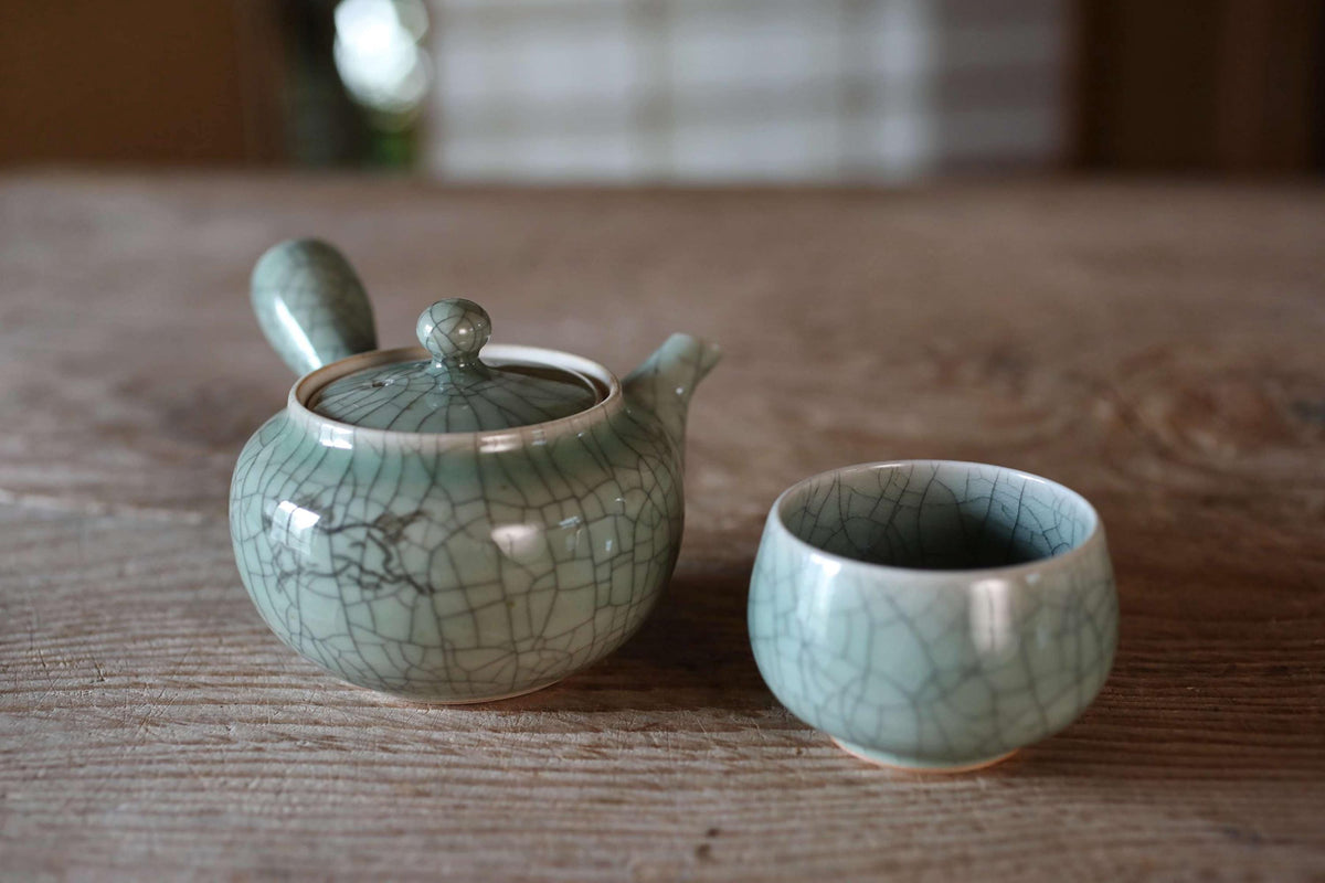 A ceramic teapot and a small cup sit on a wooden surface, creating a serene and inviting tea setting.