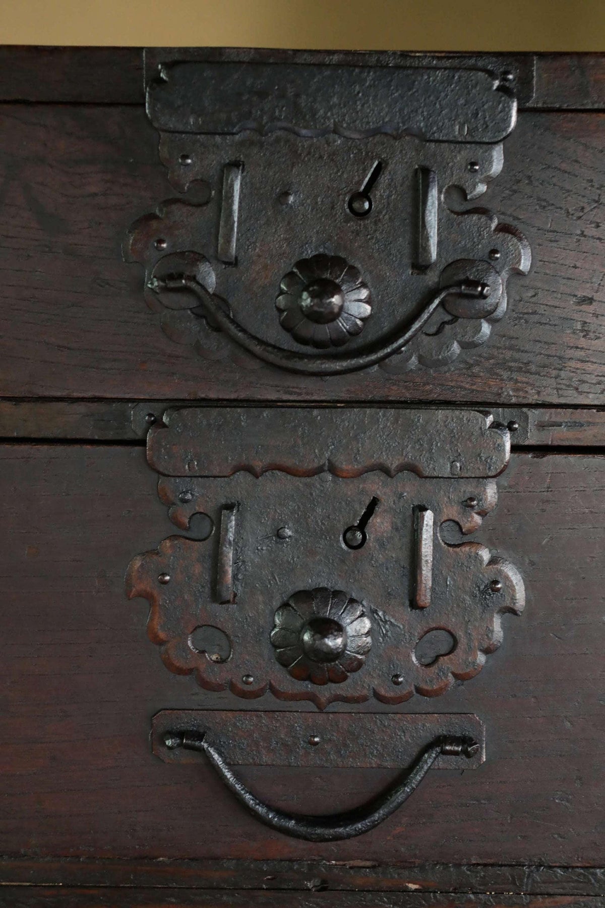 a close-up view of a dark wooden chest with intricate metal hardware, including a handle and a lock, giving it a vintage and antique appearance.