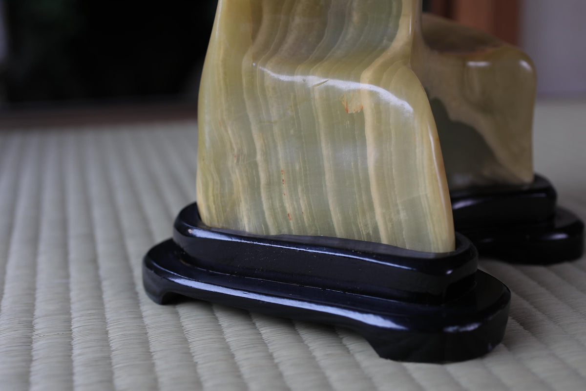 a close-up view of a yellowish-green stone or stone carving, placed on a black stand or base.