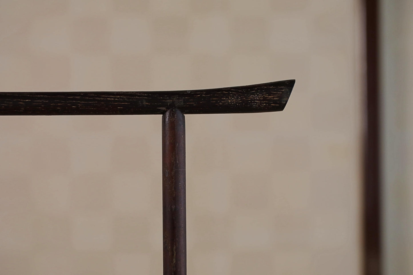 A close-up view of a dark wooden object, possibly a piece of furniture or a tool, with a blurred background.