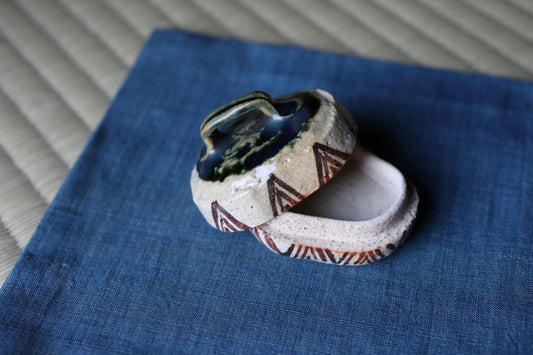 A ceramic container with a lid and a decorative pattern on the side, placed on a blue fabric surface.