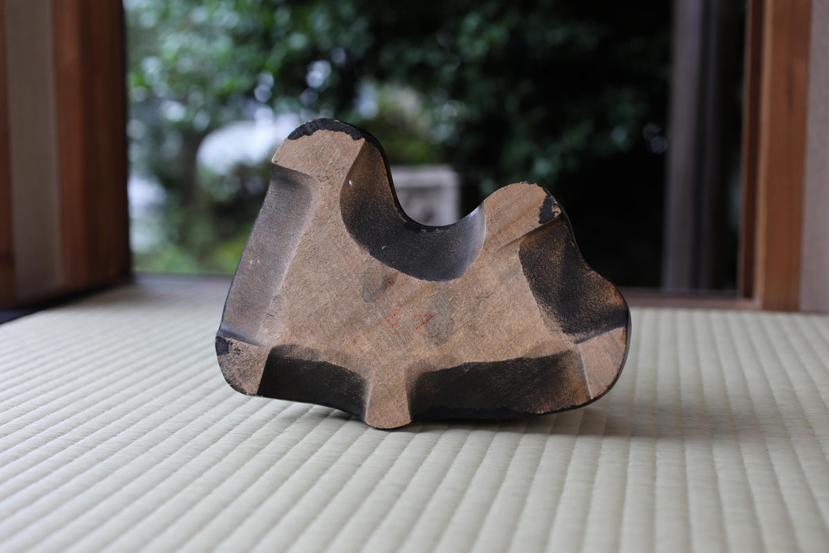 a wooden object, possibly a sculpture or a piece of furniture, sitting on a white surface.