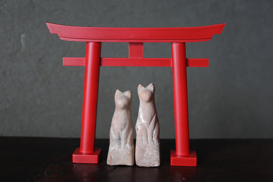 two small statues of cats standing in front of a red torii gate.