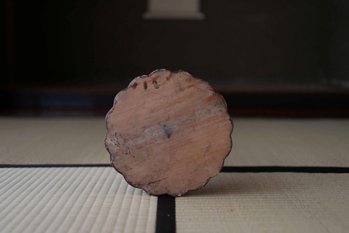 A wooden object with a scalloped edge is placed on a white mat with black lines, creating a minimalist and visually appealing composition.