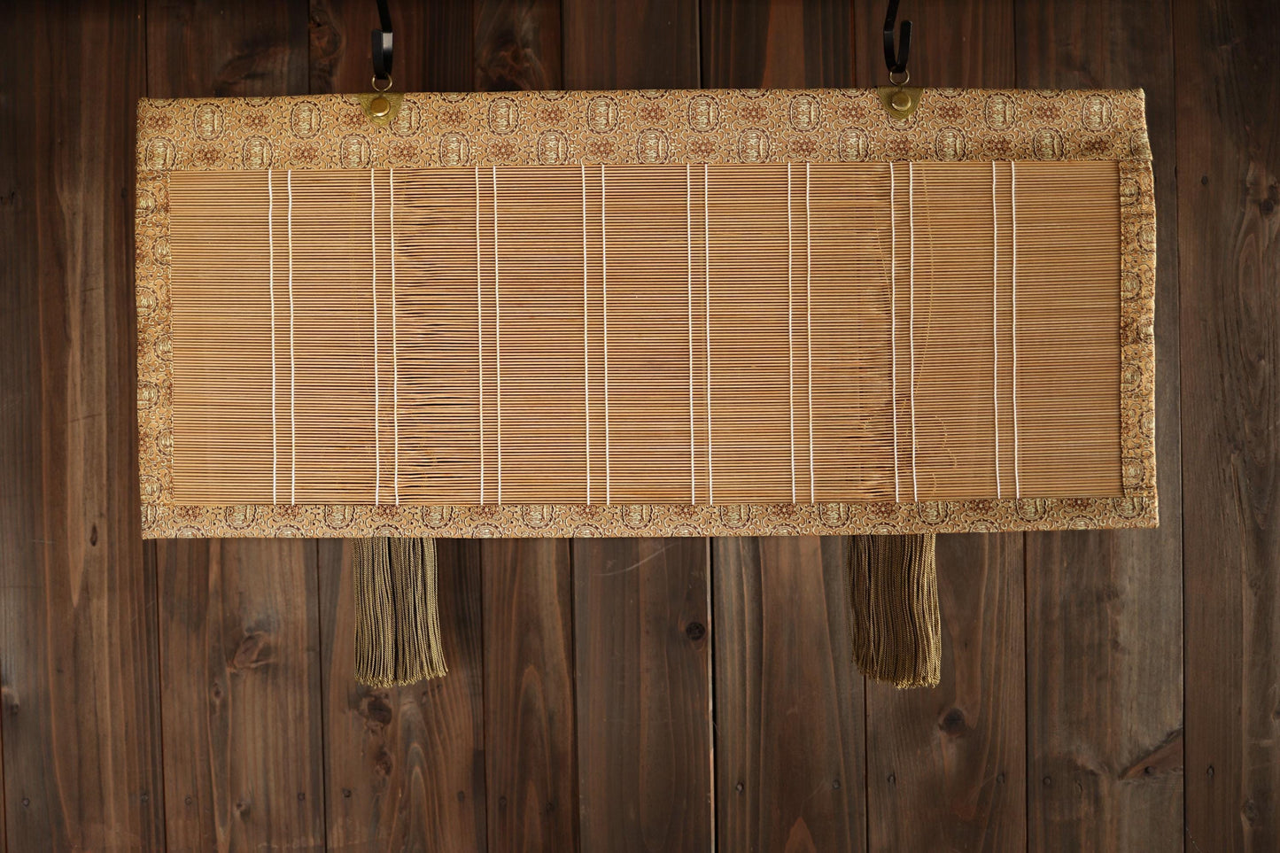A bamboo screen with a decorative border is hanging on a wooden wall.