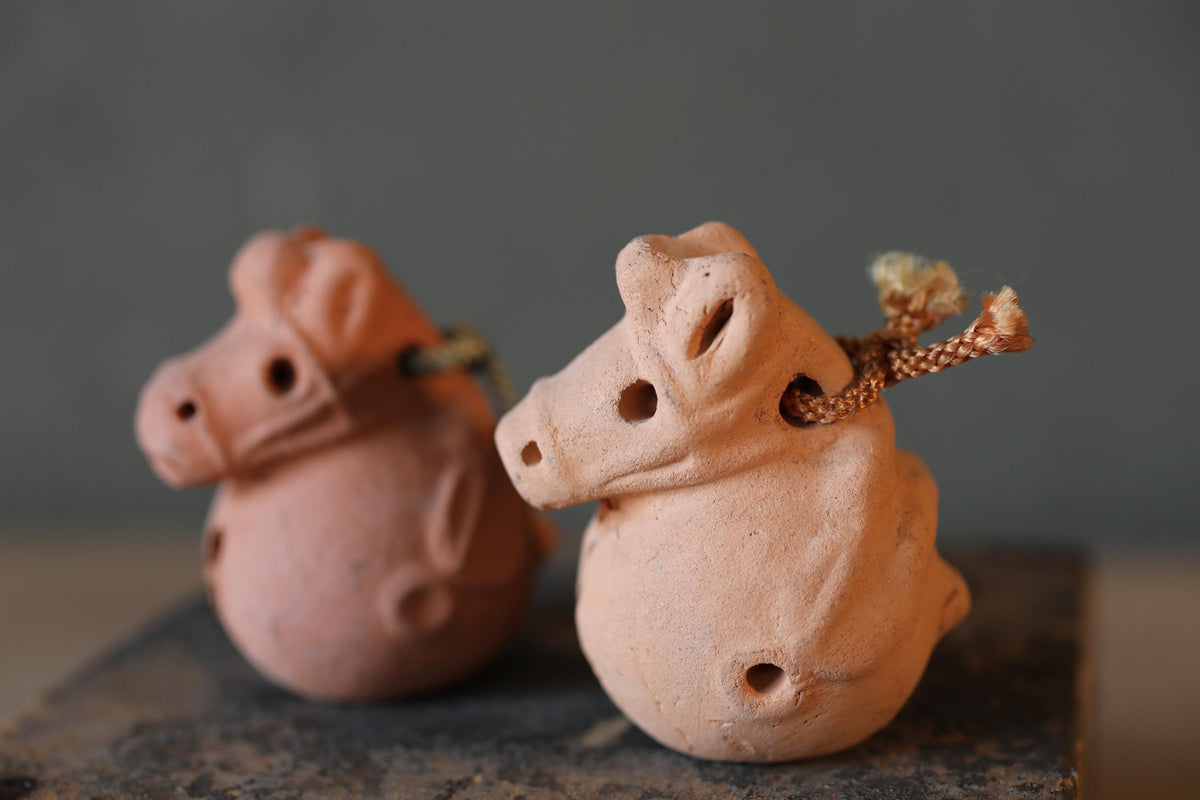 Two clay figurines of animals, possibly pigs, sitting on a dark surface.