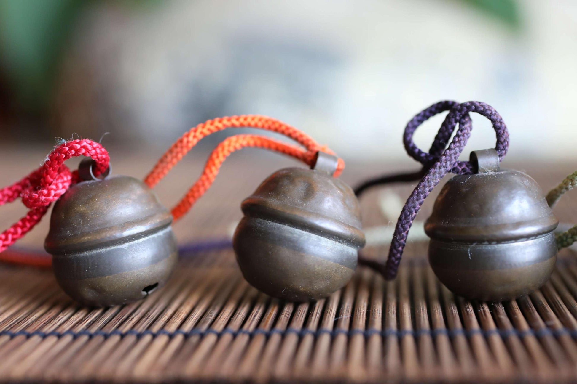 Three small, round metal bells with cords hanging from them, arranged on a wooden surface.