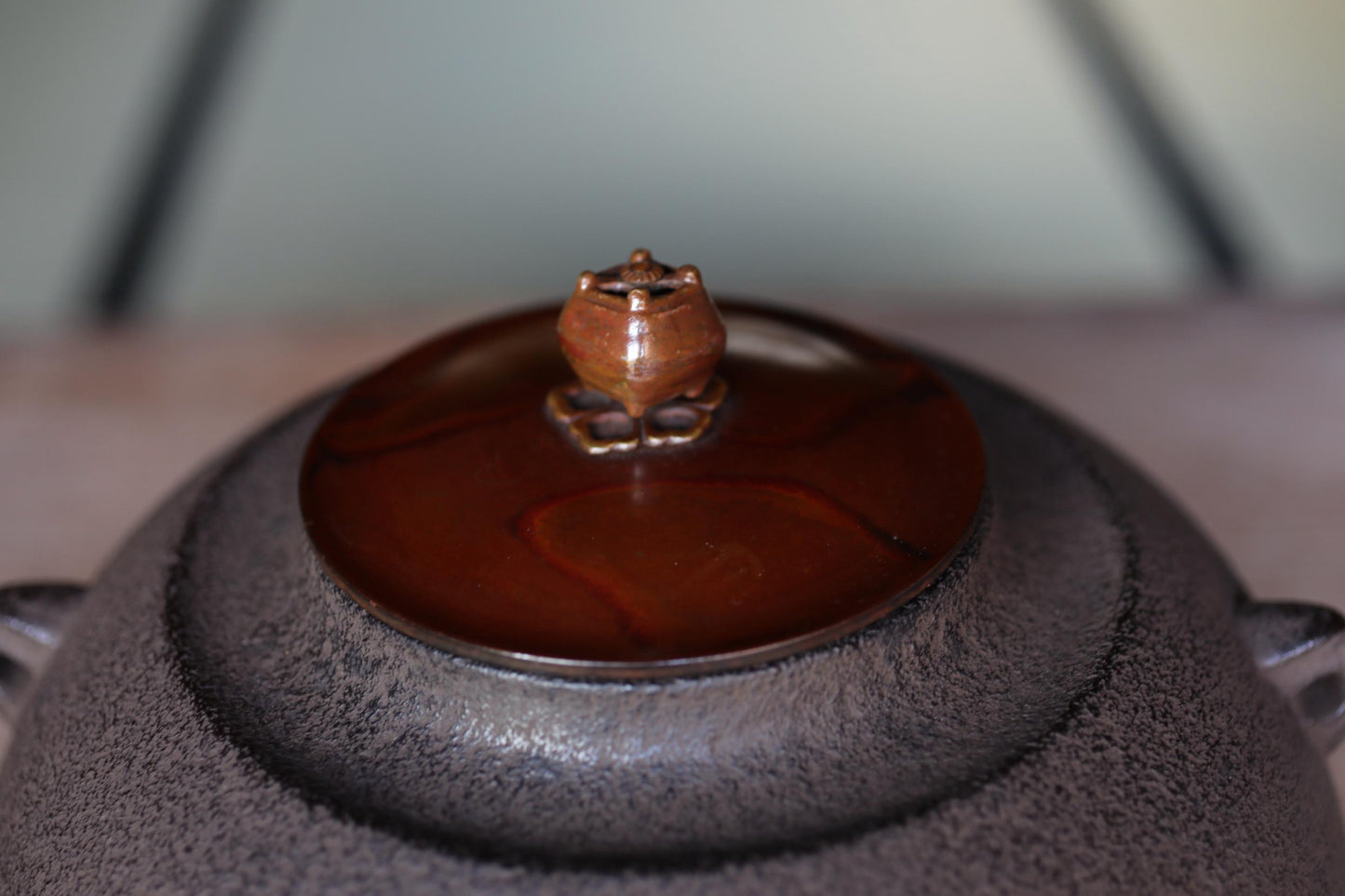 A close-up image of a dark-colored ceramic teapot with a red-brown lid and a small, ornate handle on top.