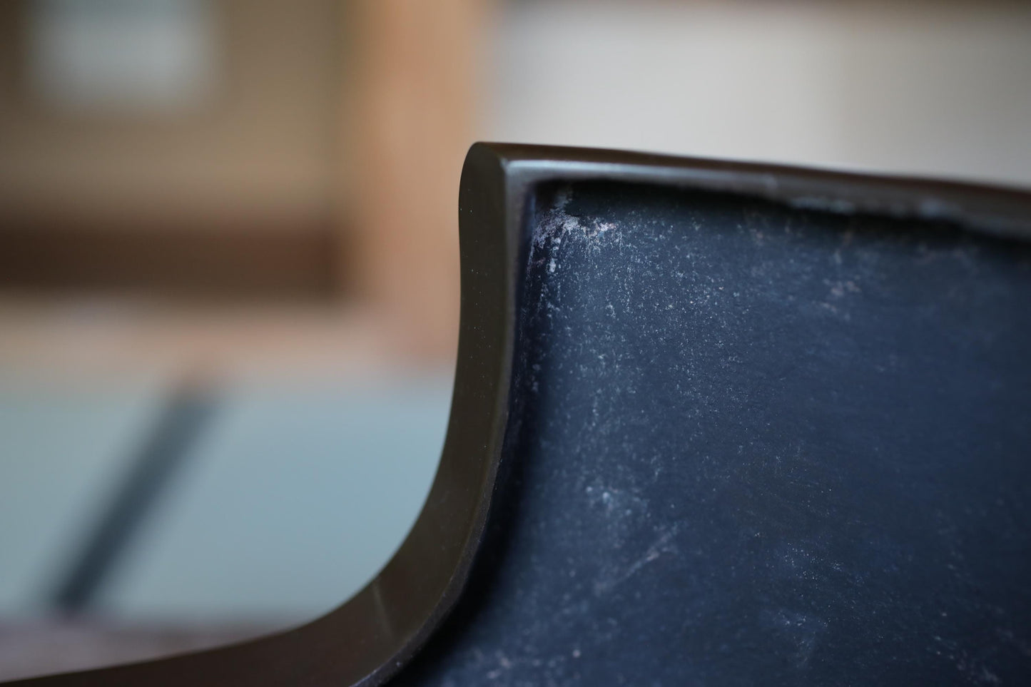 A close-up view of a dark, textured surface, possibly a piece of furniture or a wall, with a blurred background.