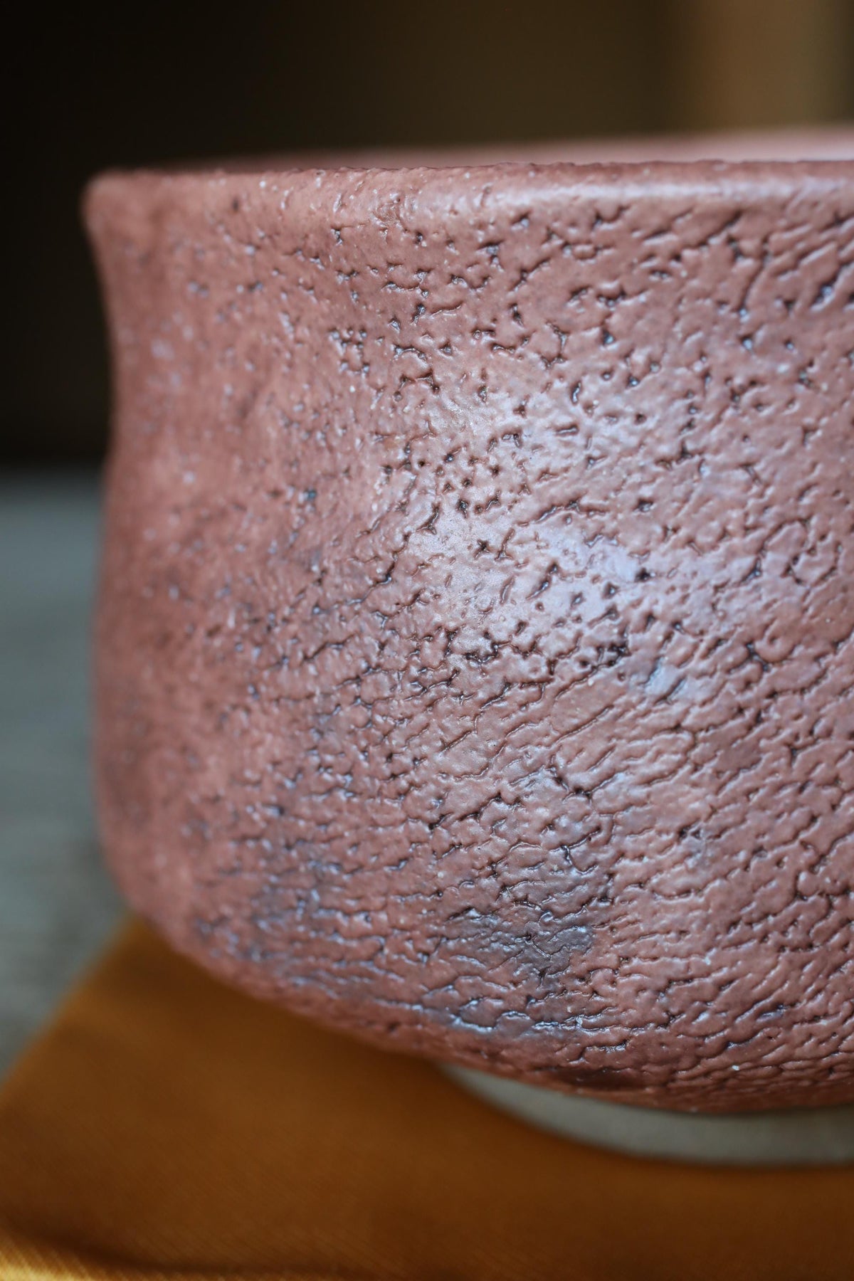 A close-up image of a textured, reddish-brown ceramic object, possibly a bowl or vase, with a rough, uneven surface.