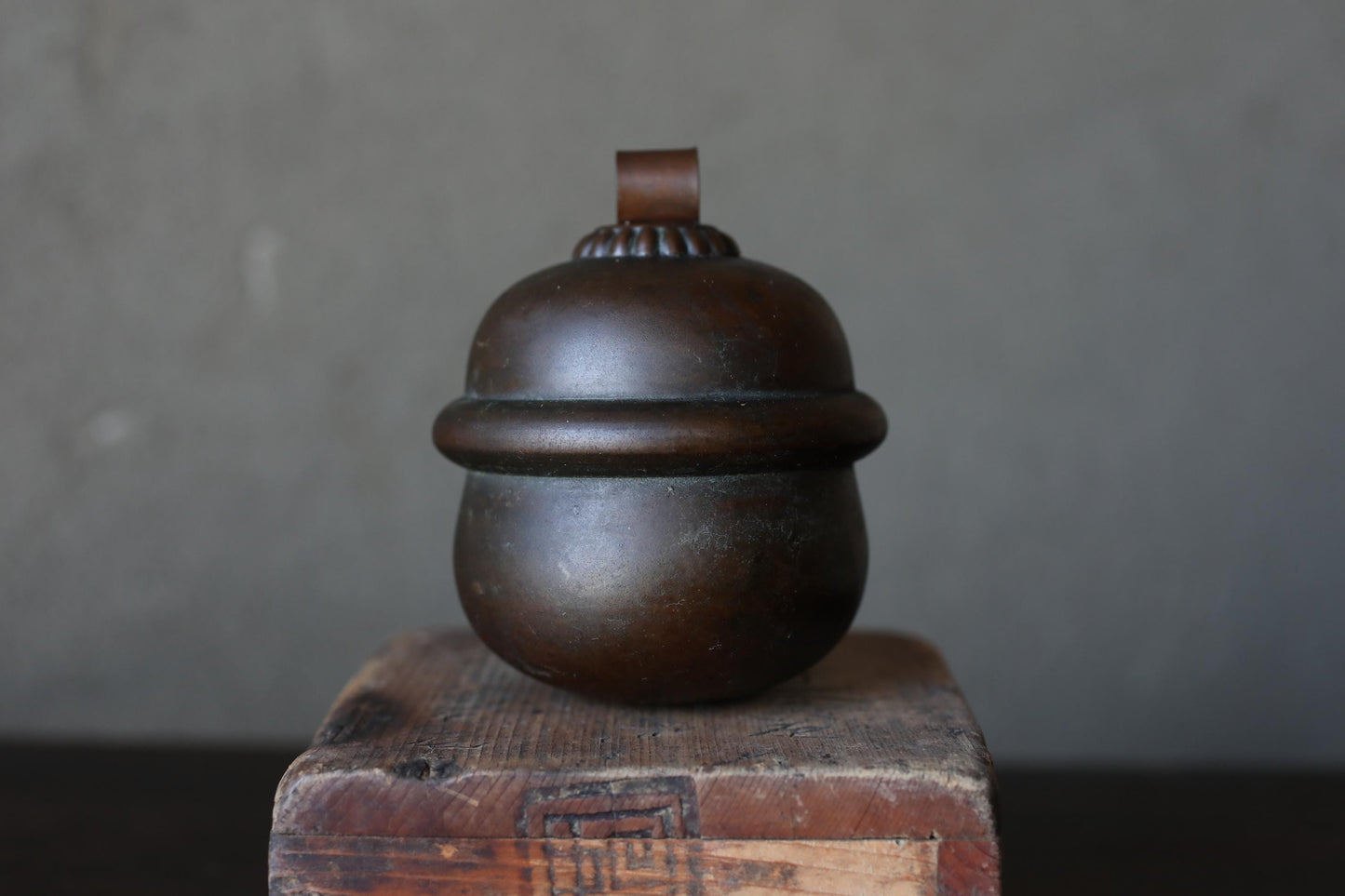 A dark brown, round metal object with a curved top sits on a wooden surface against a gray background.