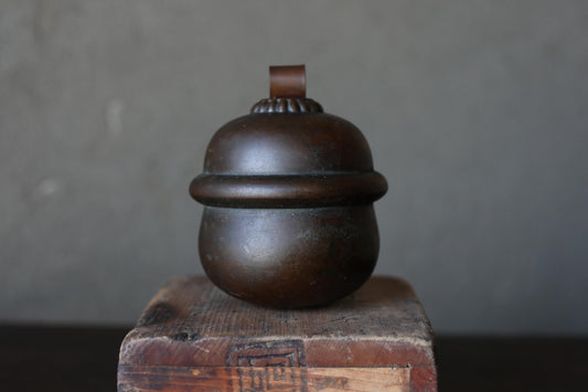A dark brown, round metal object with a curved top sits on a wooden surface against a gray background.