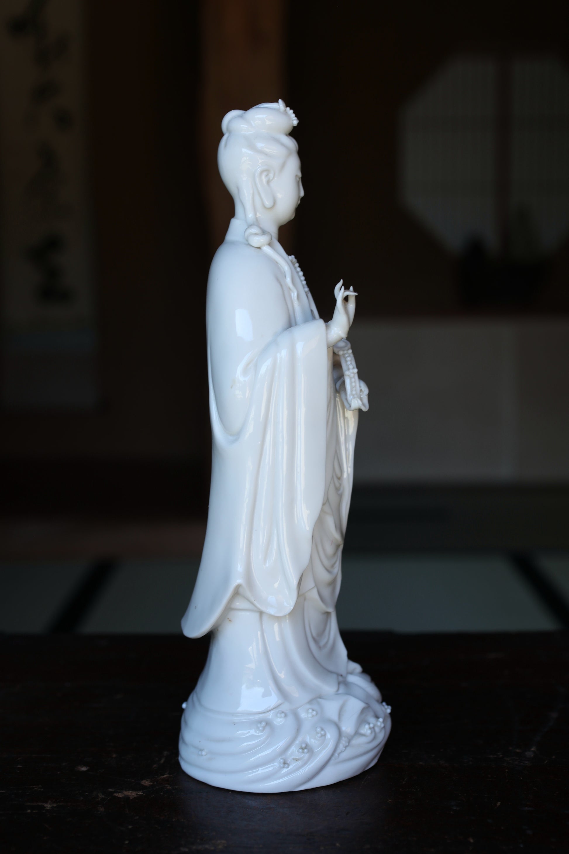 A white ceramic statue of a female deity, possibly a goddess, standing on a wooden surface.