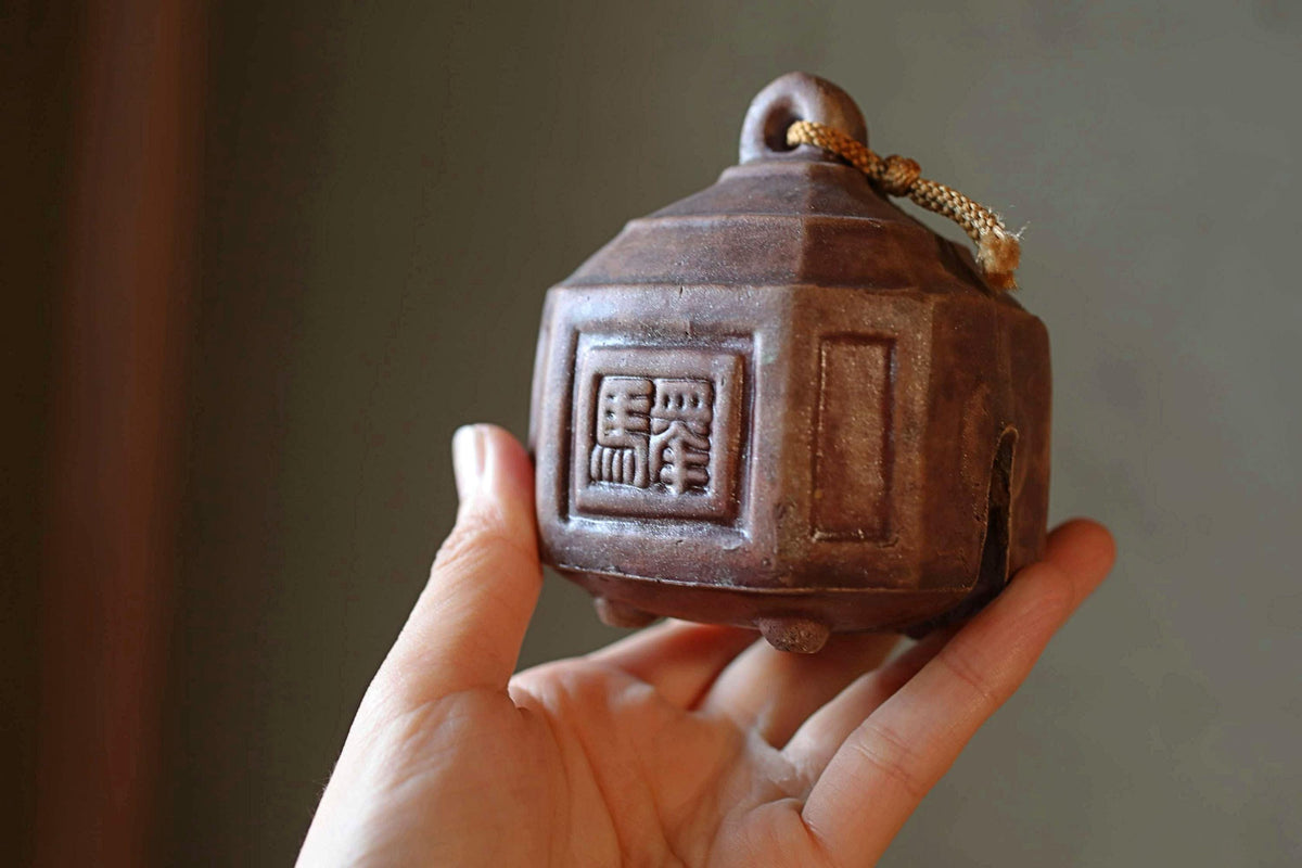 A hand holding a brown ceramic bell with an Asian character on it.