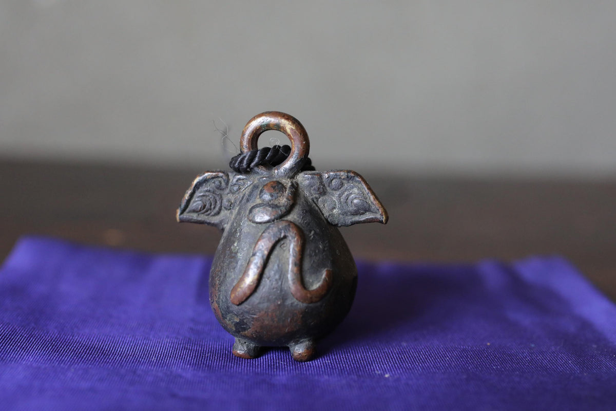 A small, ornate metal bell in the shape of a pig sits on a blue cloth.