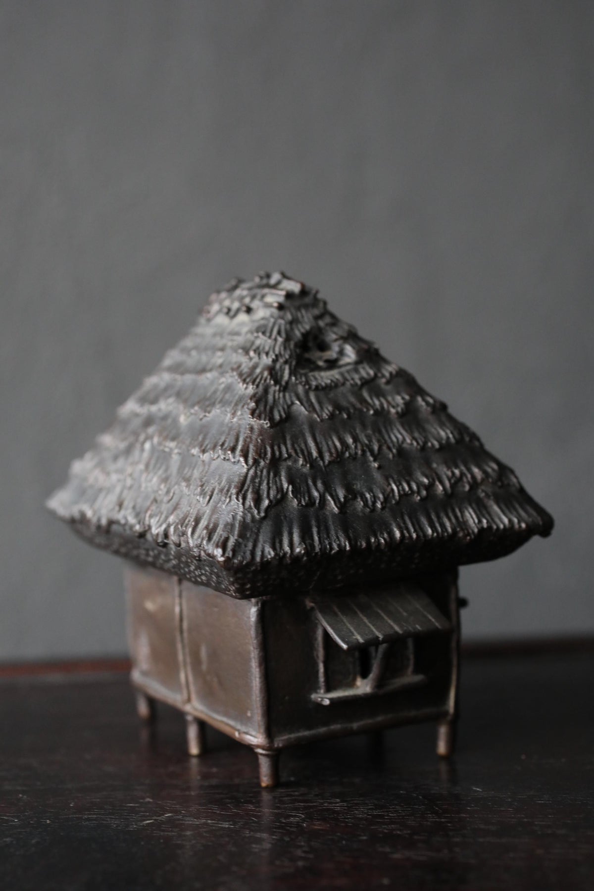 A small, intricately designed metal sculpture of a thatched roof hut sits on a dark surface.