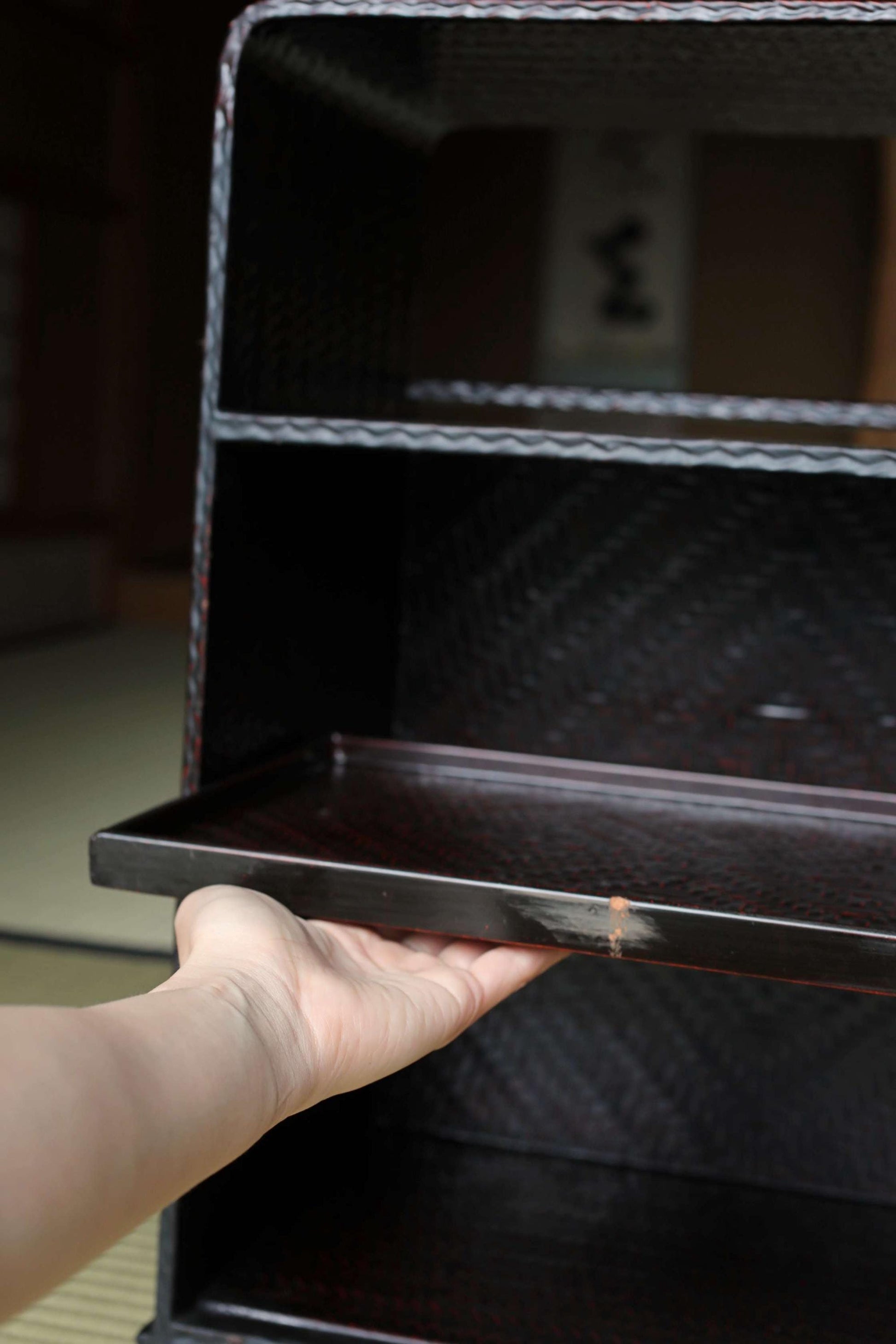 A hand is holding a black tray with a wicker pattern, placed on a dark surface.