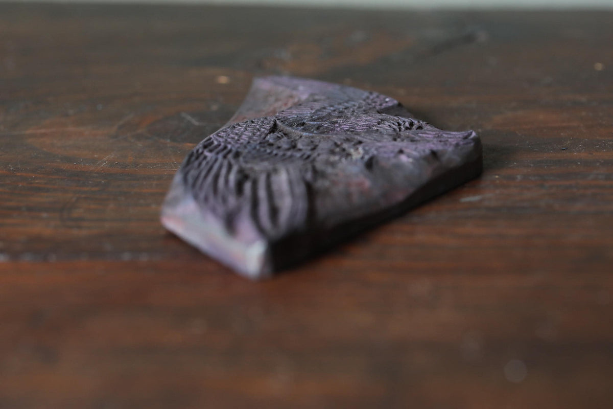 A dark purple, ornate object with a textured surface is resting on a wooden surface.