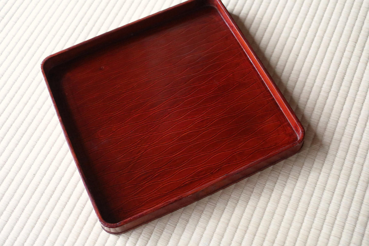 A red, square-shaped tray with a wavy pattern on its surface, placed on a white surface.
