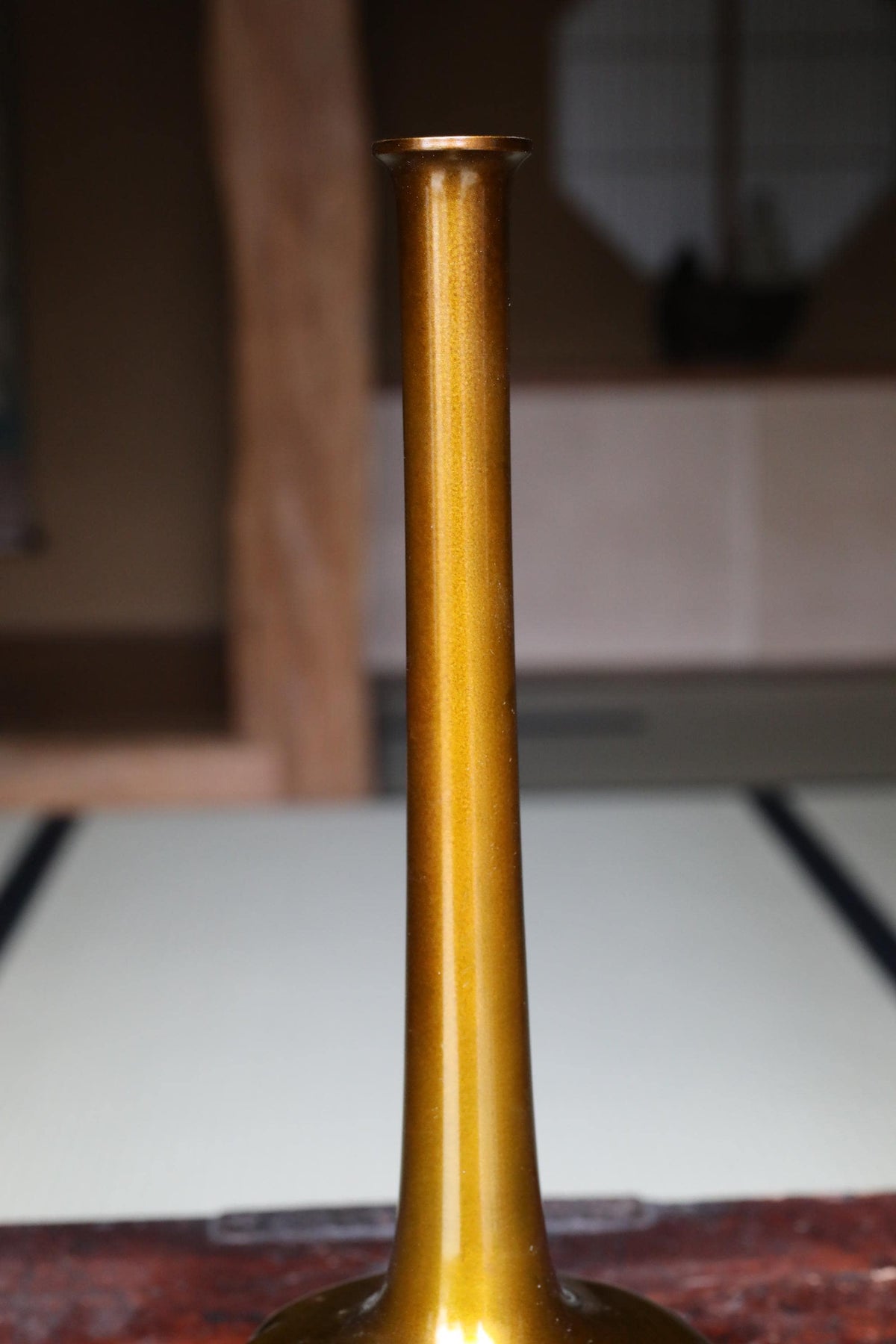 A golden vase with a shiny, reflective surface sits on a wooden surface.