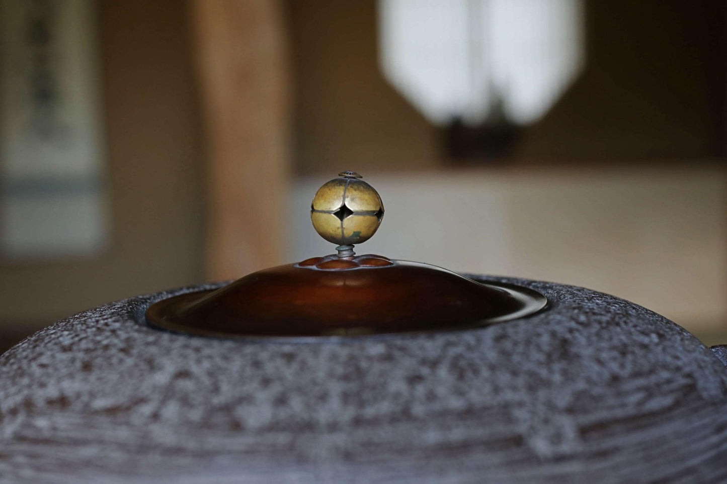 A close-up view of a dark-colored ceramic object, possibly a vase or bowl, with a golden-colored ball or ornament on top.