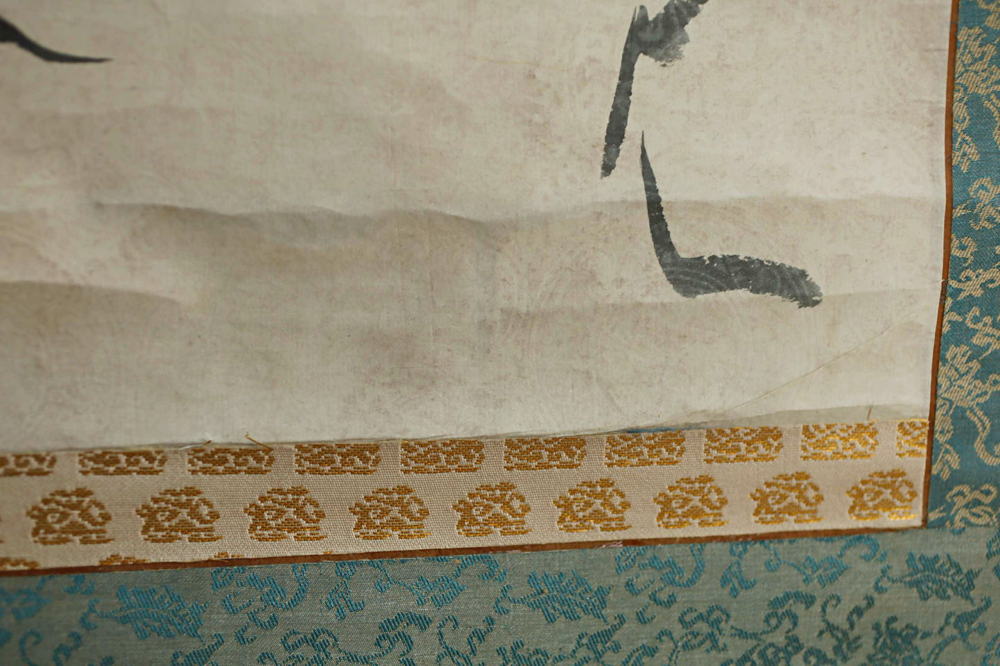 a close-up view of a piece of artwork, possibly a painting or drawing, with a patterned border and a white background. The artwork appears to be a decorative piece, possibly a wall hanging or a framed print, with a gold and white patterned border. The artwork is set against a blue and white patterned background, creating a visually appealing contrast.