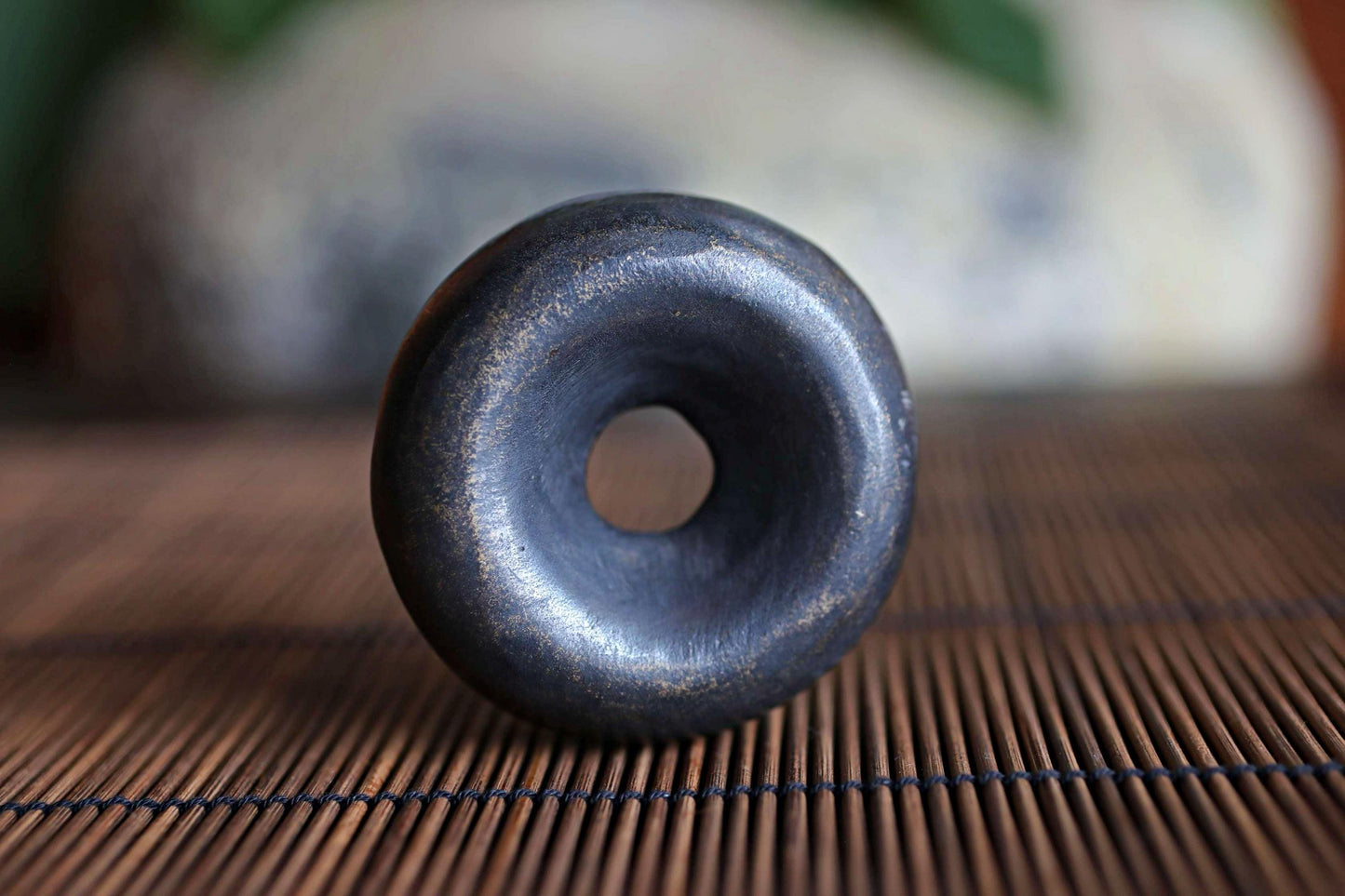 A close-up image of a black, round object with a hole in the center, resting on a bamboo mat.
