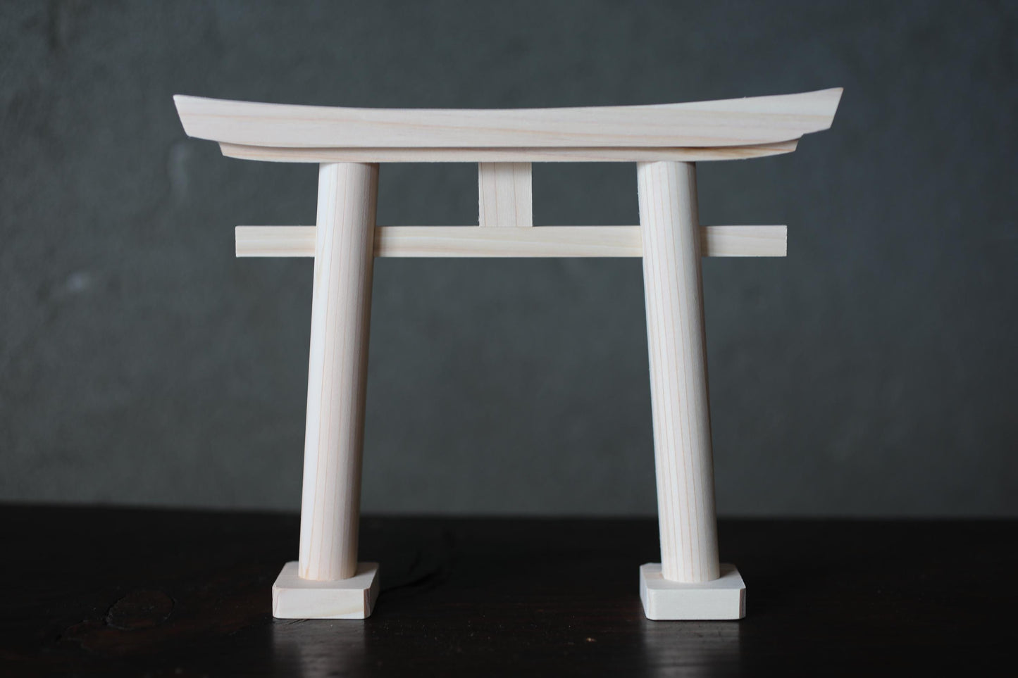 A wooden torii gate, a traditional Japanese gate, is shown against a dark background.