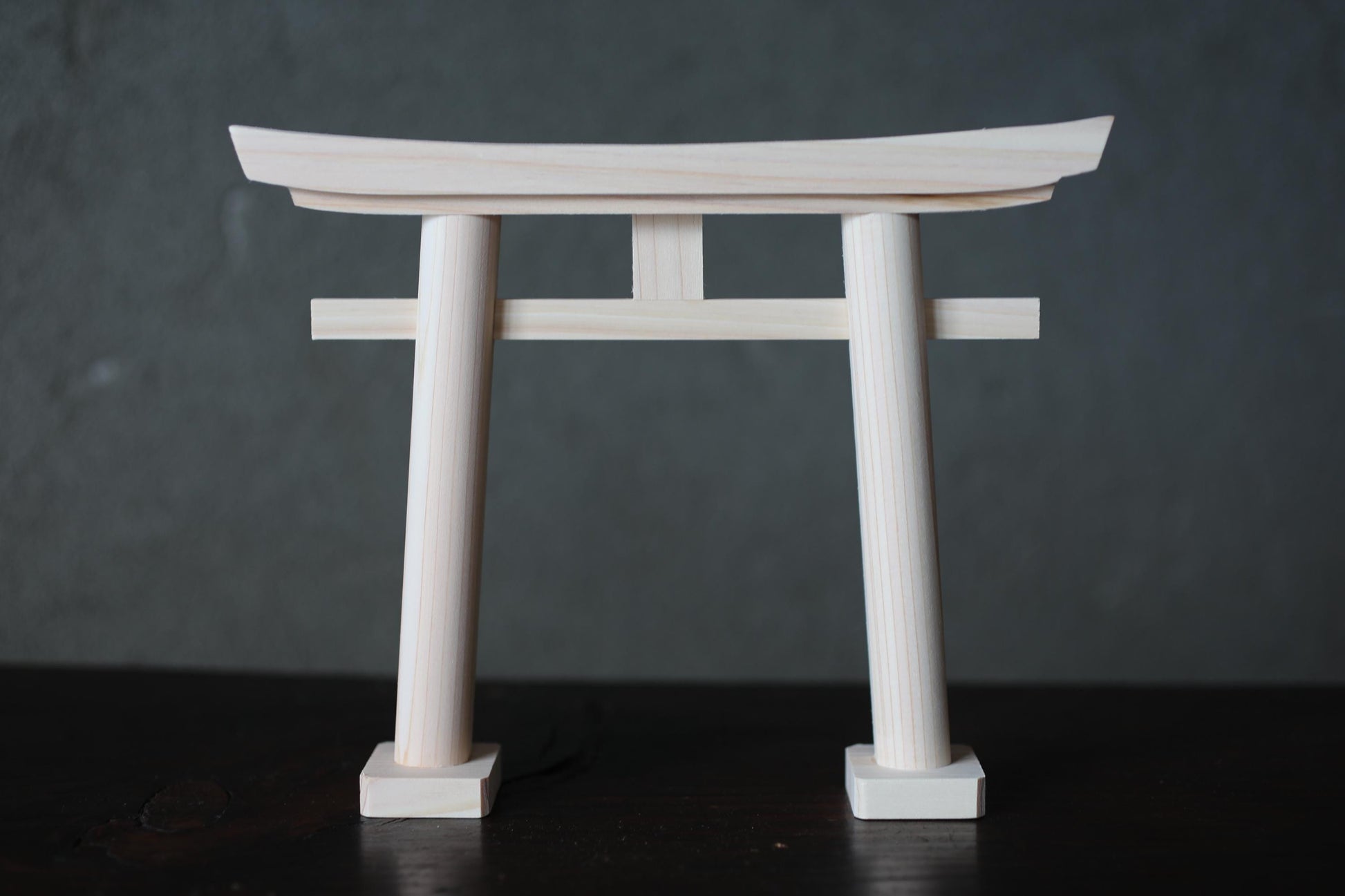 A wooden torii gate, a traditional Japanese gate, is shown against a dark background.