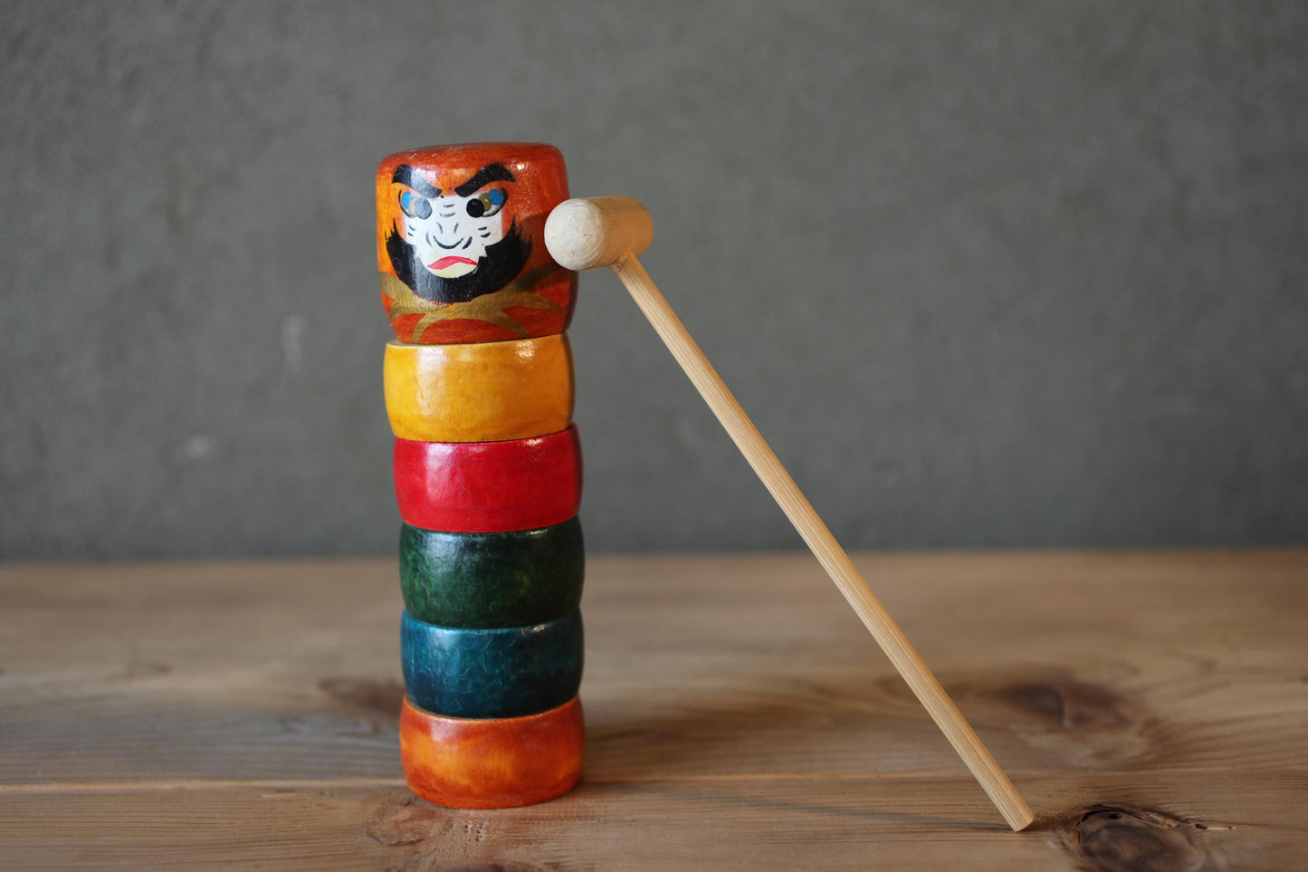 A stack of colorful wooden rings with a wooden stick leaning against a gray wall.