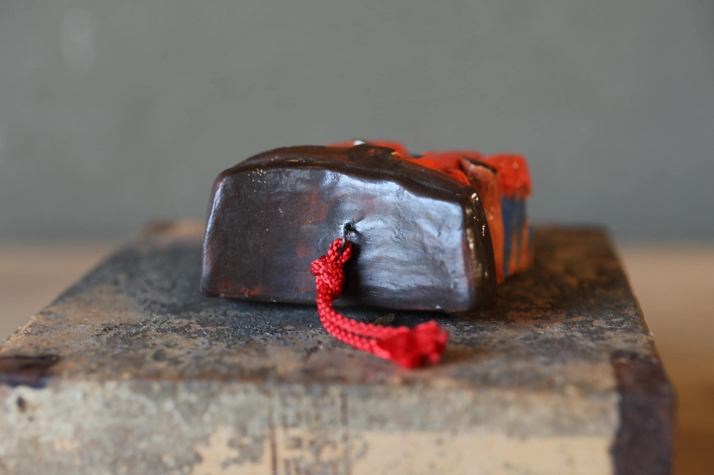 A dark brown ceramic object with a red string attached to it, sitting on a wooden surface.