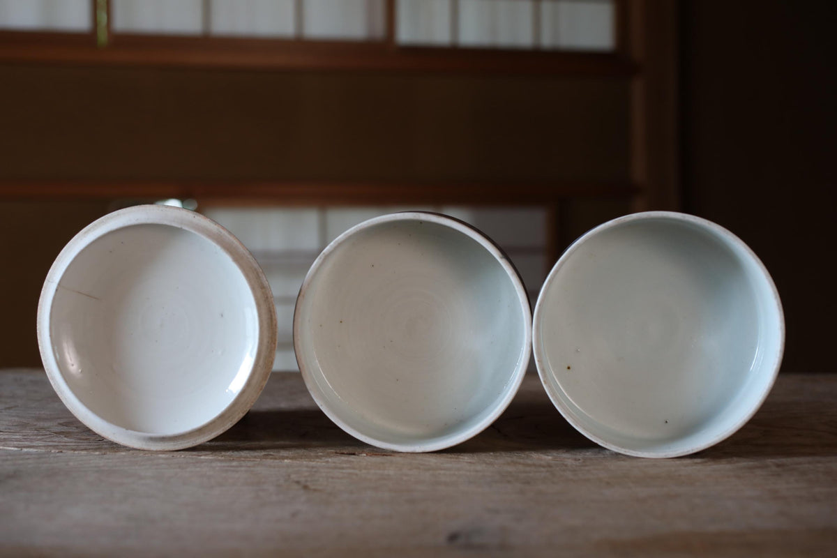 Three white ceramic bowls are arranged on a wooden surface, with the middle bowl slightly larger than the other two.