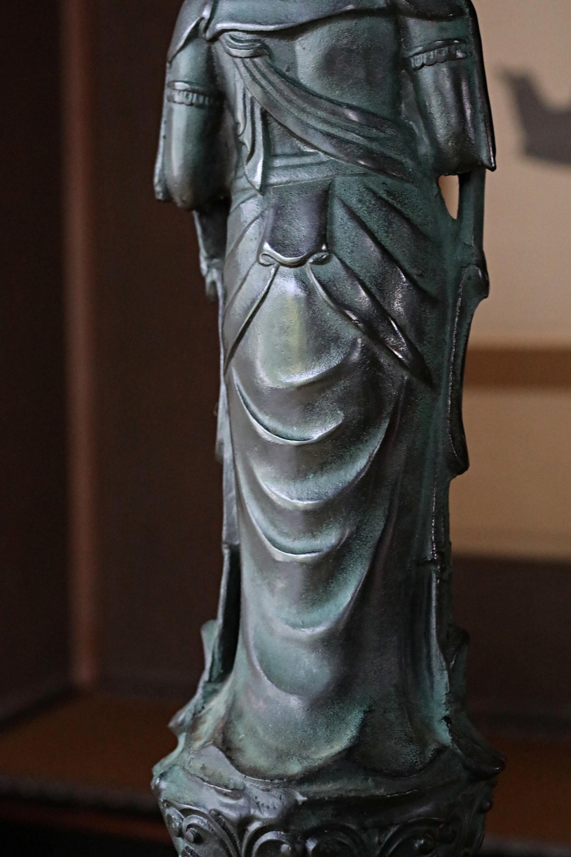 A close-up view of a bronze statue of a person, likely a religious figure, with intricate details and flowing robes.