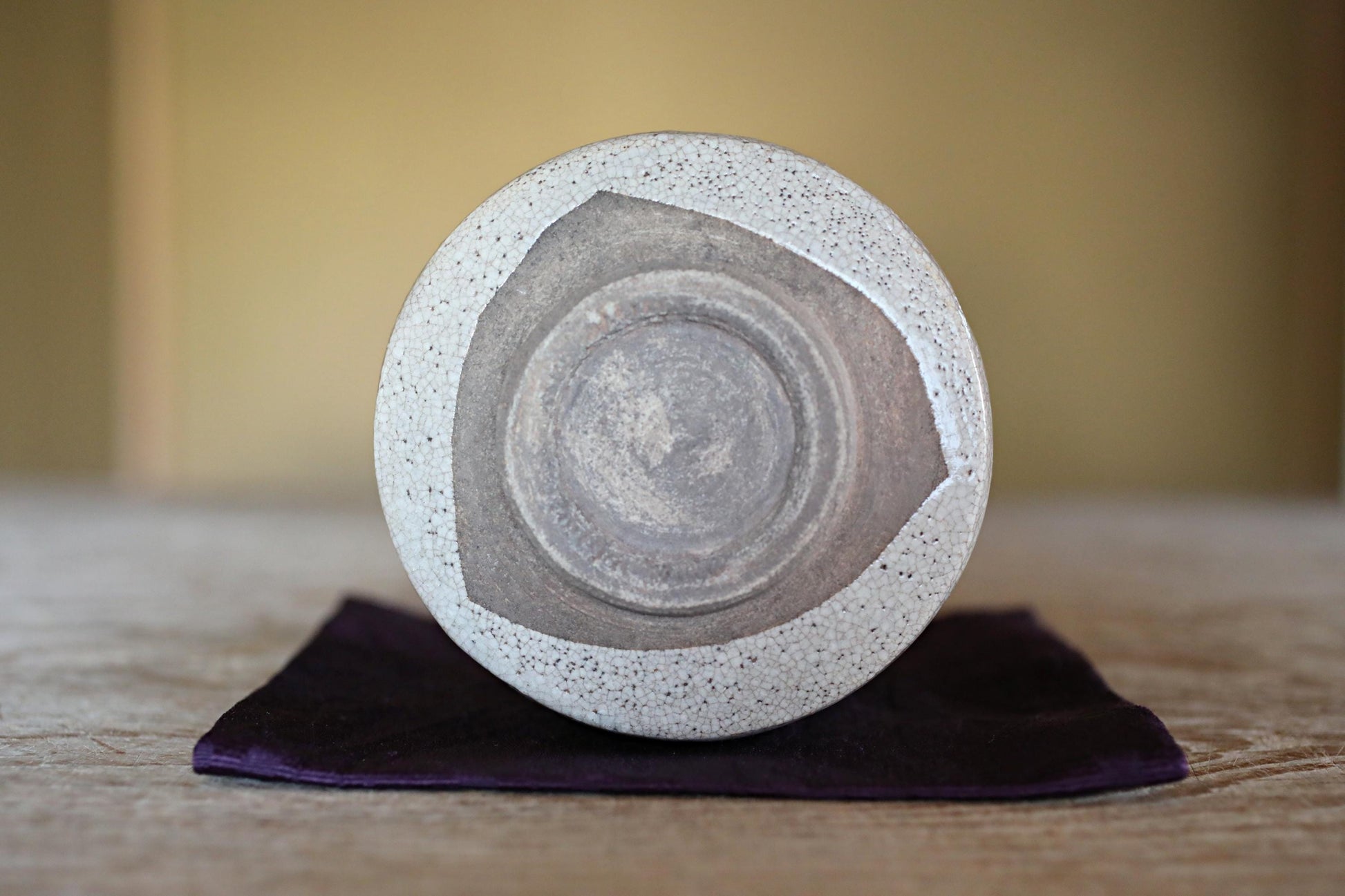 A white ceramic bowl with a speckled pattern sits on a purple cloth on a wooden surface.
