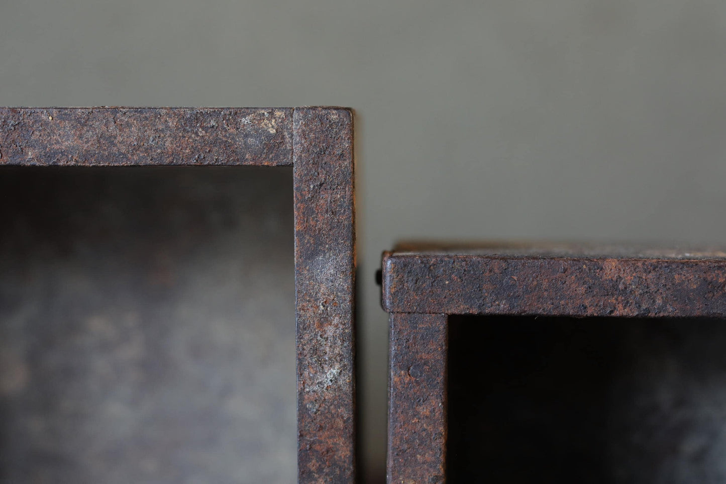 two rusted metal boxes with visible signs of wear and tear, set against a grey background.