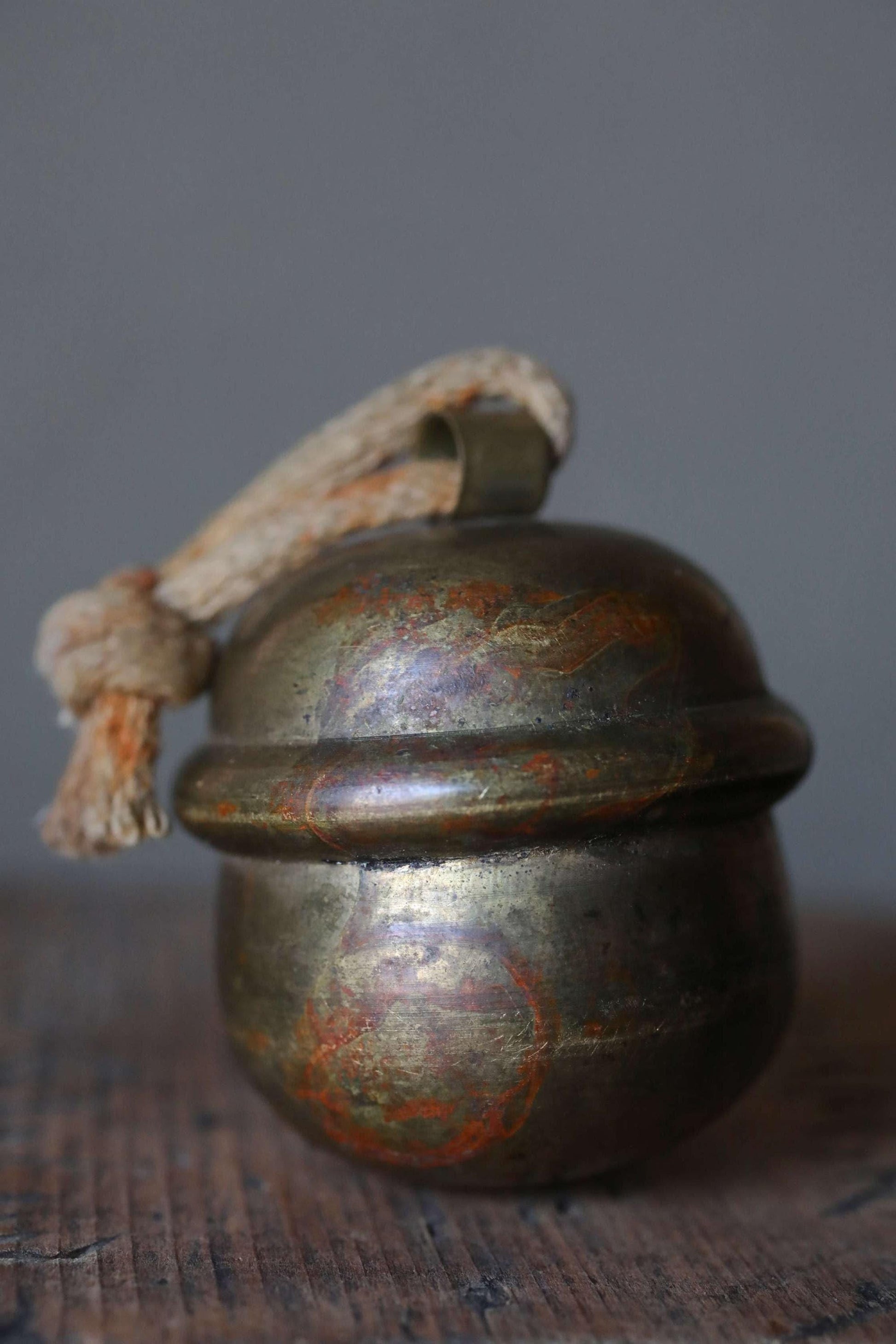 An old, rusted metal bell with a rope hanging from it, sitting on a wooden surface.