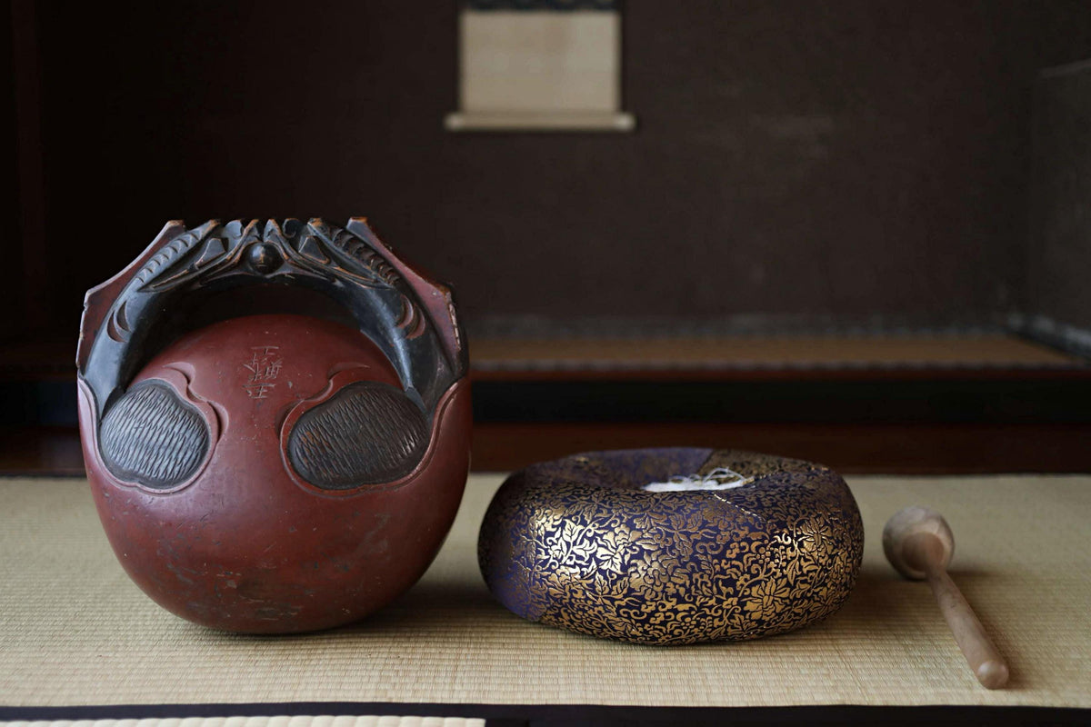 two decorative ceramic objects, one red and one gold, placed on a woven mat.