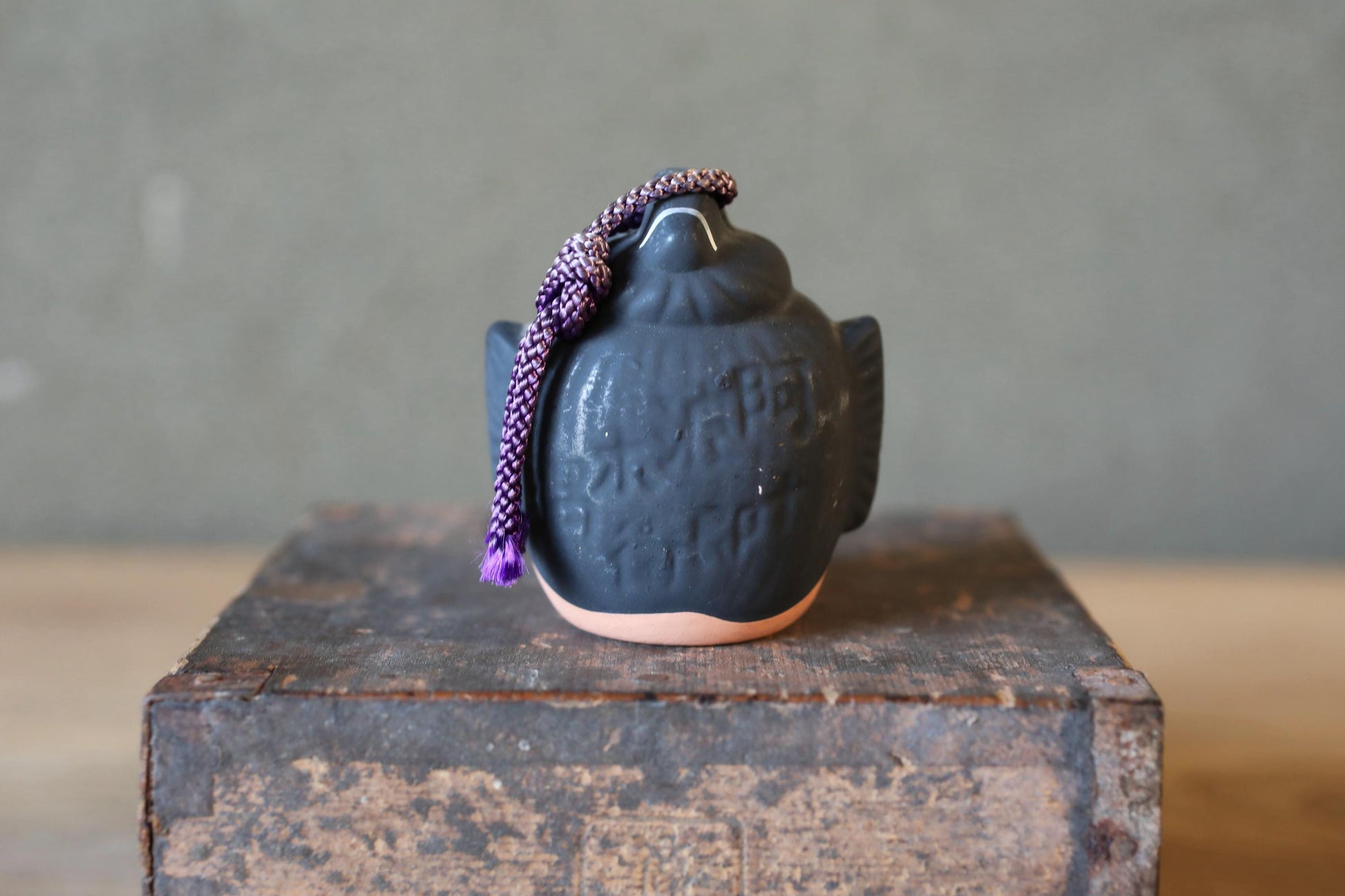 A ceramic object with a textured surface sits on a wooden surface, with a purple string hanging from it.