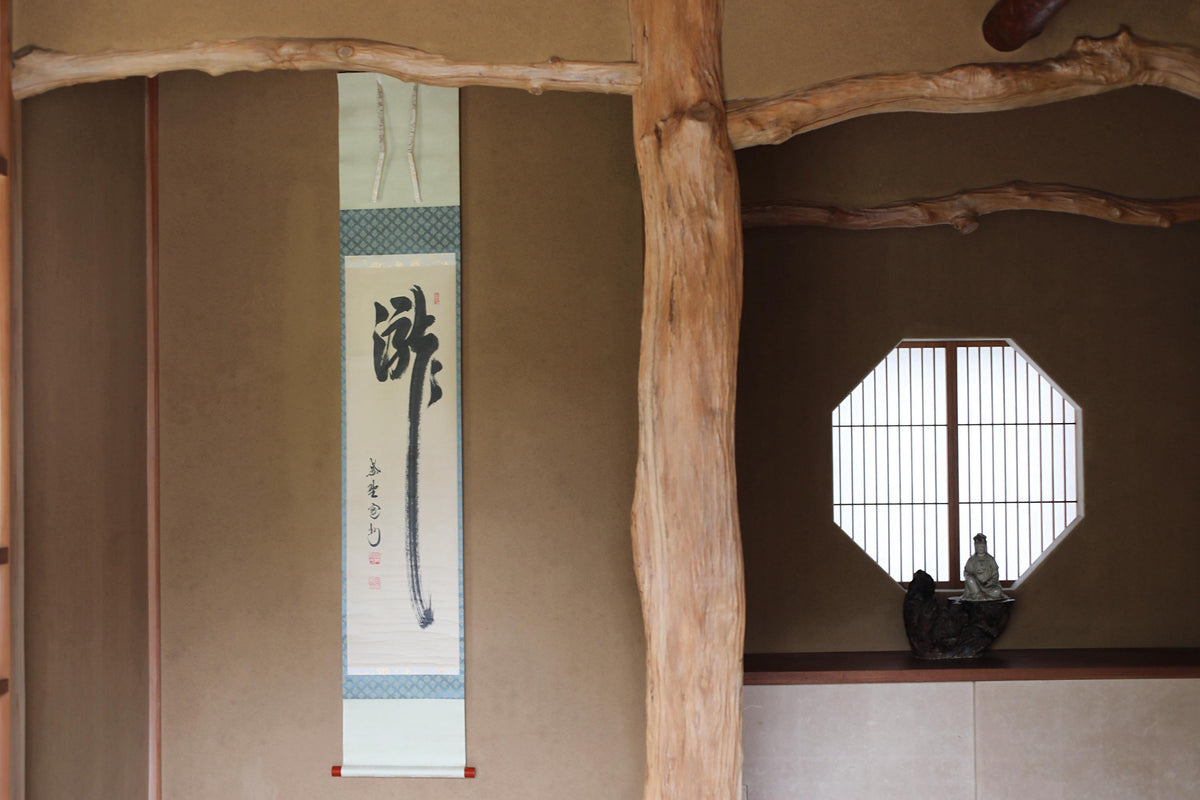 a traditional Japanese room with a wooden beam, a window with a bamboo frame, and a hanging scroll with Japanese characters.